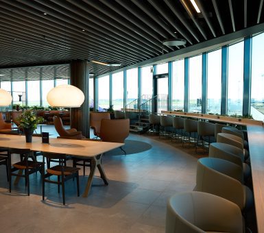 Interior of the Pearl Lounge at Copenhagen Airport with seating, communal tables and runway views through floor‑to‑ceiling windows.