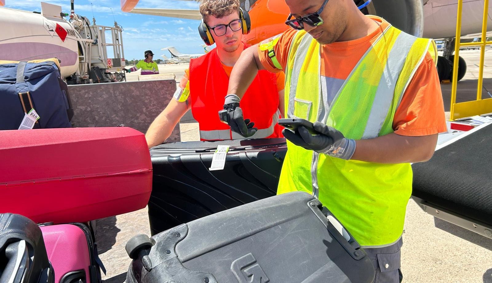 Ground crew scanning and tagging luggage beside an aircraft during apron operations.