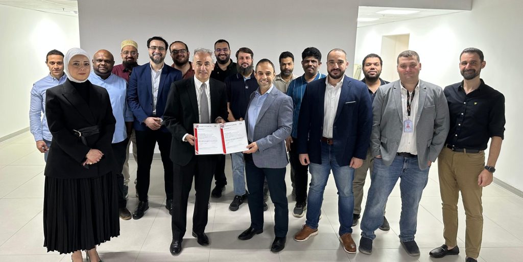 Kuwait team members gathered indoors holding an ISO certification document.
