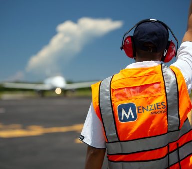 Menzies Aviation ground handling team member directing an aircraft on the airport apron.