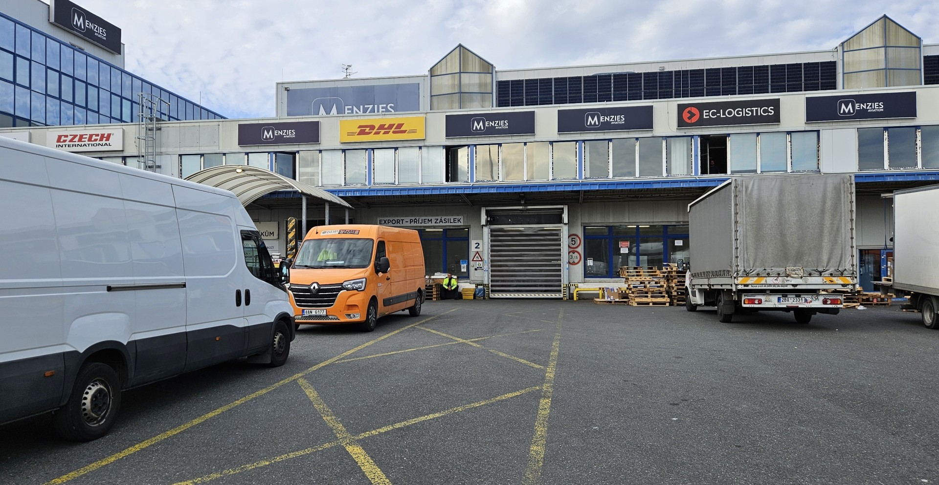 Menzies Aviation cargo facility in Prague with trucks and delivery vans outside the warehouse.